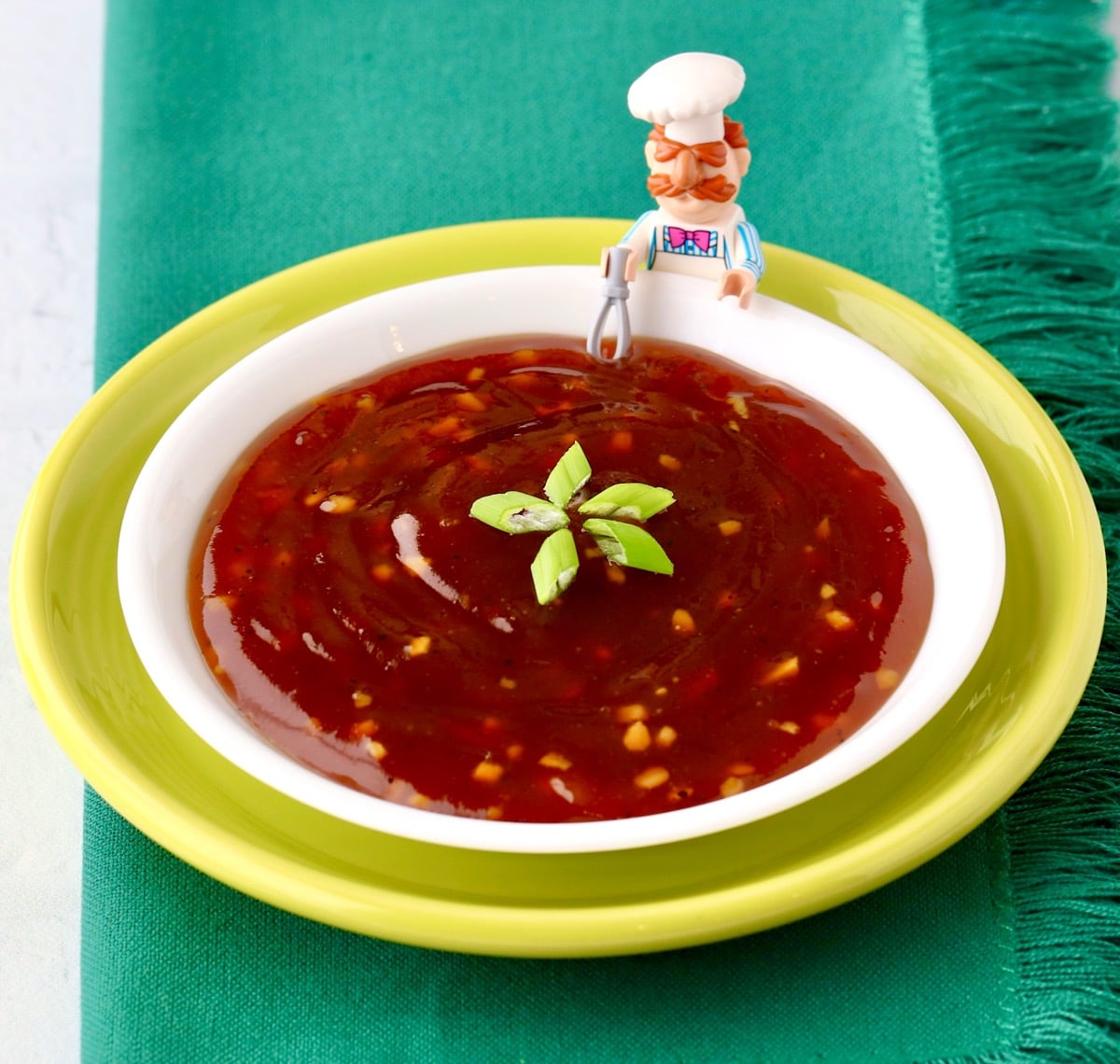 Homemade teriyaki sauce in bowl garnished with green onions, and lego chef with whisk to the side.