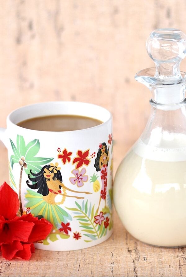 Homemade vanilla coffee creamer in glass container next to mug with coffee.