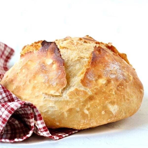 Loaf of homemade artisan bread with dish towel to the side.