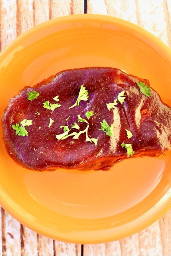 Barbecue pork chop on orange plate.