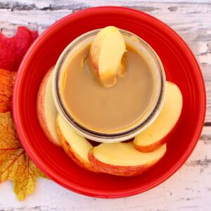 Caramel sauce in small jar surrounded by apple slices.