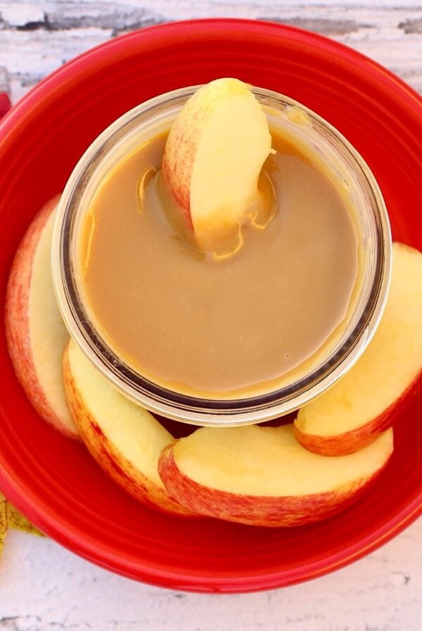 Caramel sauce in small jar surrounded by apple slices.