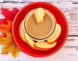Caramel sauce in mason jar surrounded by apple slices.