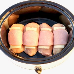 Chicken cordon bleu pieces in crock pot with cheese and ham on top.