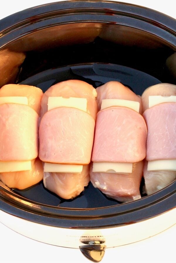 Chicken cordon bleu pieces in crock pot with cheese and ham on top.