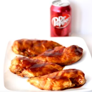 Four pieces of Dr Pepper BBQ Sauce chicken on plate with can of Dr. Pepper in background.