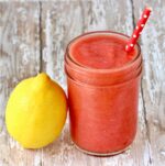 Frozen strawberry lemonade in mason jar with lemon to the side.