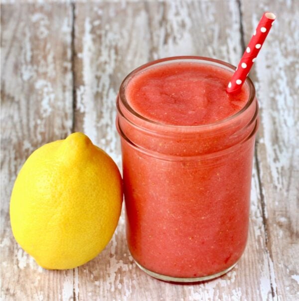Frozen strawberry lemonade in mason jar with lemon to the side.