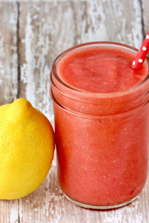 Frozen strawberry lemonade in mason jar with lemon to the side.