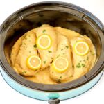Four pieces of chicken in crockpot topped with lemon garlic sauce, lemon slices and parsley.
