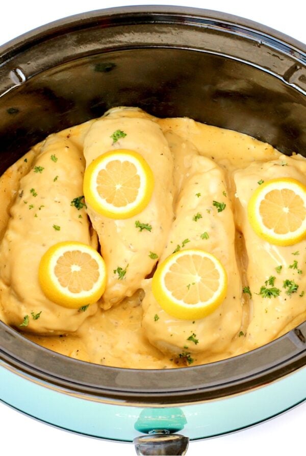 Four pieces of chicken in crockpot topped with lemon garlic sauce, lemon slices and parsley.