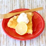 Slice of lemon pie on plate with whip cream on top.