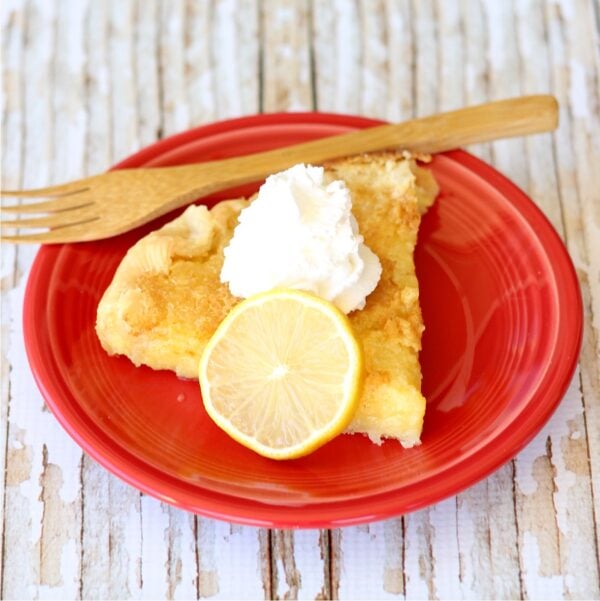 Slice of lemon pie on plate with whip cream on top.