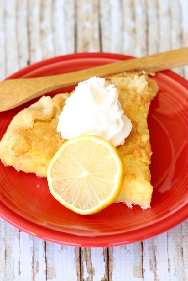 Slice of lemon pie on plate with whip cream on top.