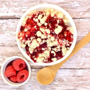 Raspberry dump cake in bowl with fresh raspberries and spoon to the side.