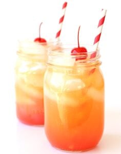 Two Shirley temple mocktails in mason jars, each with a cherry on top.