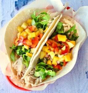 Two shredded chicken tacos in basket with lettuce and pineapple mango salsa on top.