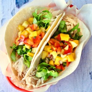 Two shredded chicken tacos in basket with lettuce and pineapple mango salsa on top.