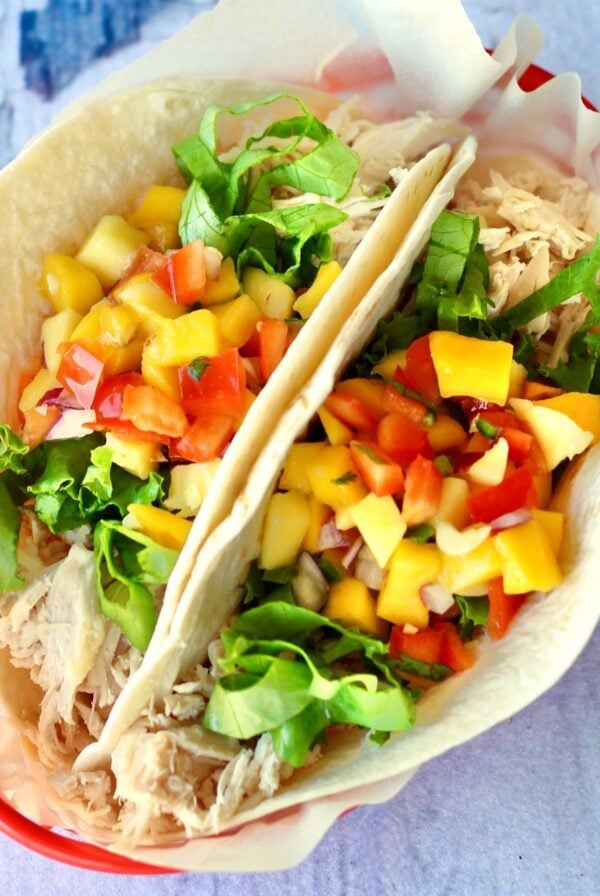 Two shredded chicken tacos in basket with lettuce and pineapple mango salsa on top.