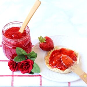 Homemade strawberry jam for canning in mason jar with spoon, and spread on English muffin.
