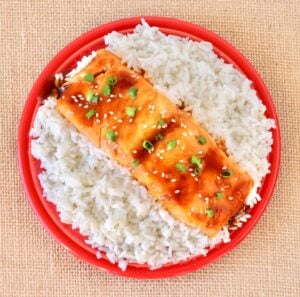 Teriyaki salmon filet on plate filled with rice.