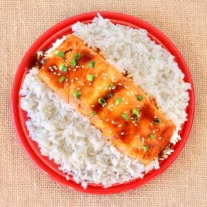Teriyaki salmon filet on plate filled with rice.