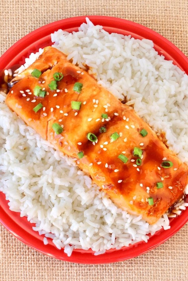 Teriyaki salmon filet on plate filled with rice.