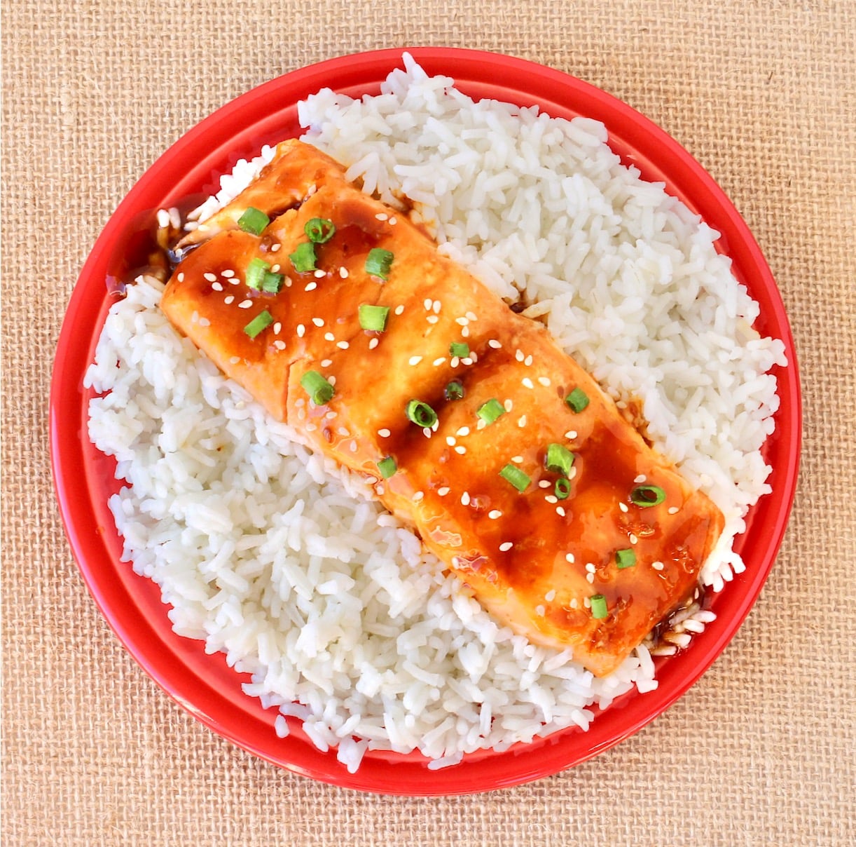 Teriyaki salmon filet on plate filled with rice.