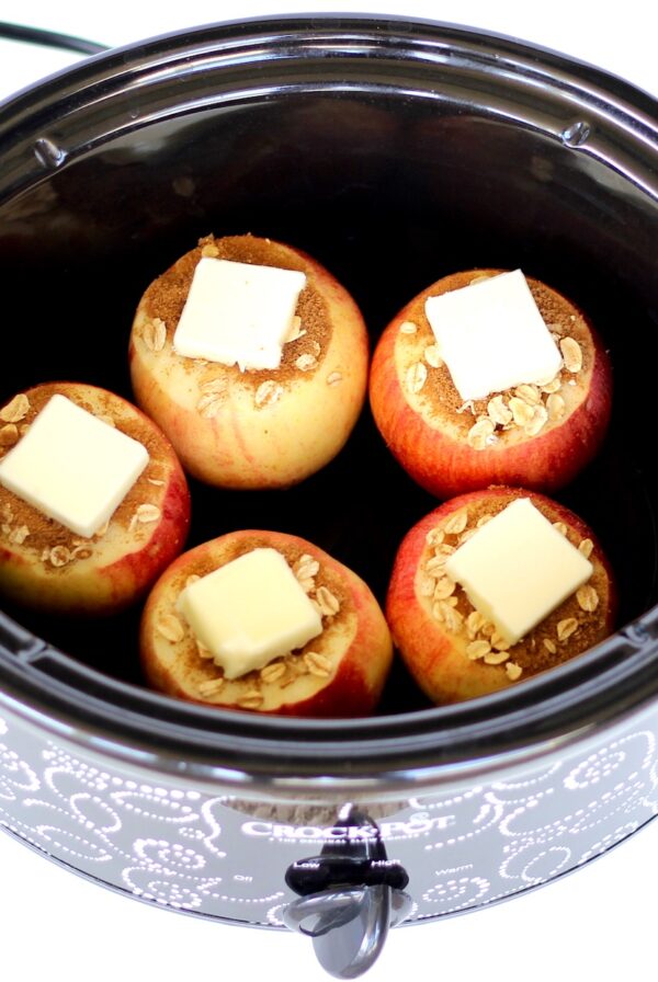 Five apples with cinnamon, butter, and oats ready to be baked in crockpot.