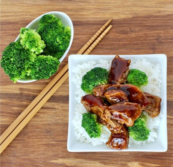 Beef and broccoli on plate with rice, and chopsticks to the side.