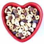 Cereal Snack mix with Cheerios, chocolate chips, raisins and nuts in heart shaped dish.