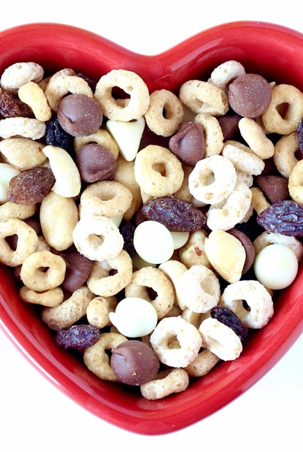 Cereal Snack mix with Cheerios, chocolate chips, raisins and nuts in heart shaped dish.