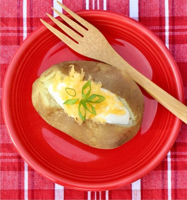 Baked potato with sour cream, shredded cheddar cheese and chives on top.