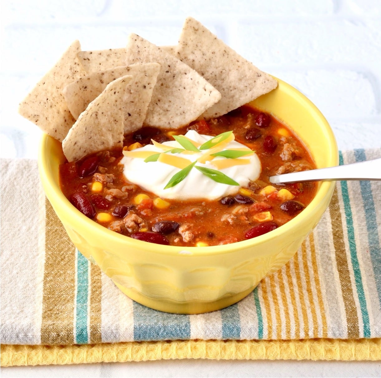 Taco soup in bowl with sour cream, cheddar cheese, and green onions on top.