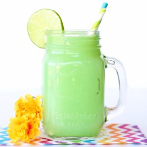 Green punch in mason jar with lime slice and straws.