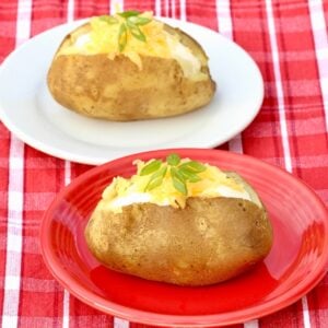 Two baked potatoes topped with sour cream, shredded cheddar cheese and green onions.