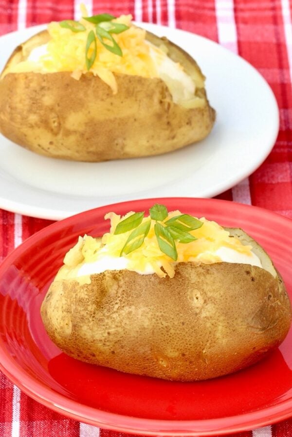 Two baked potatoes topped with sour cream, shredded cheddar cheese and green onions.