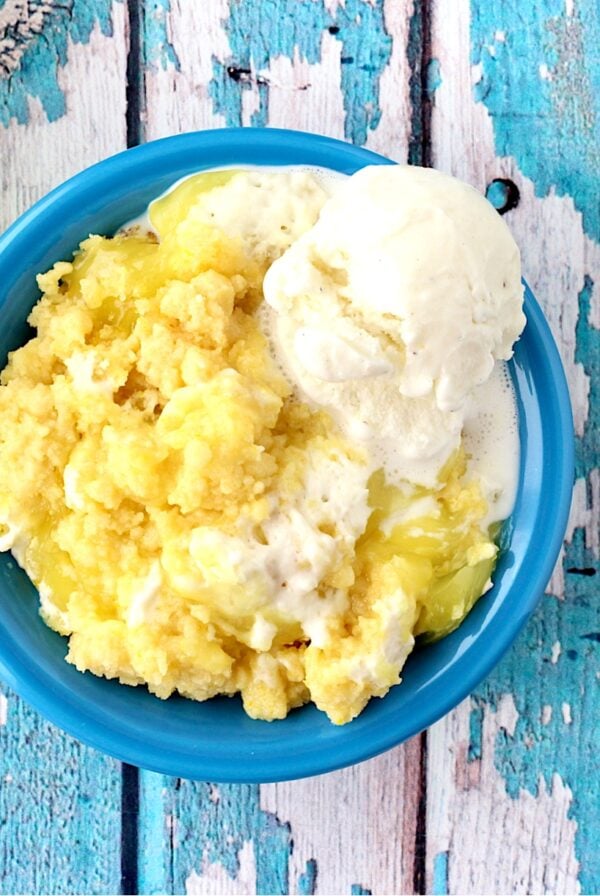 Lemon cream cheese dump cake in bowl with vanilla ice cream and spoon to the side.