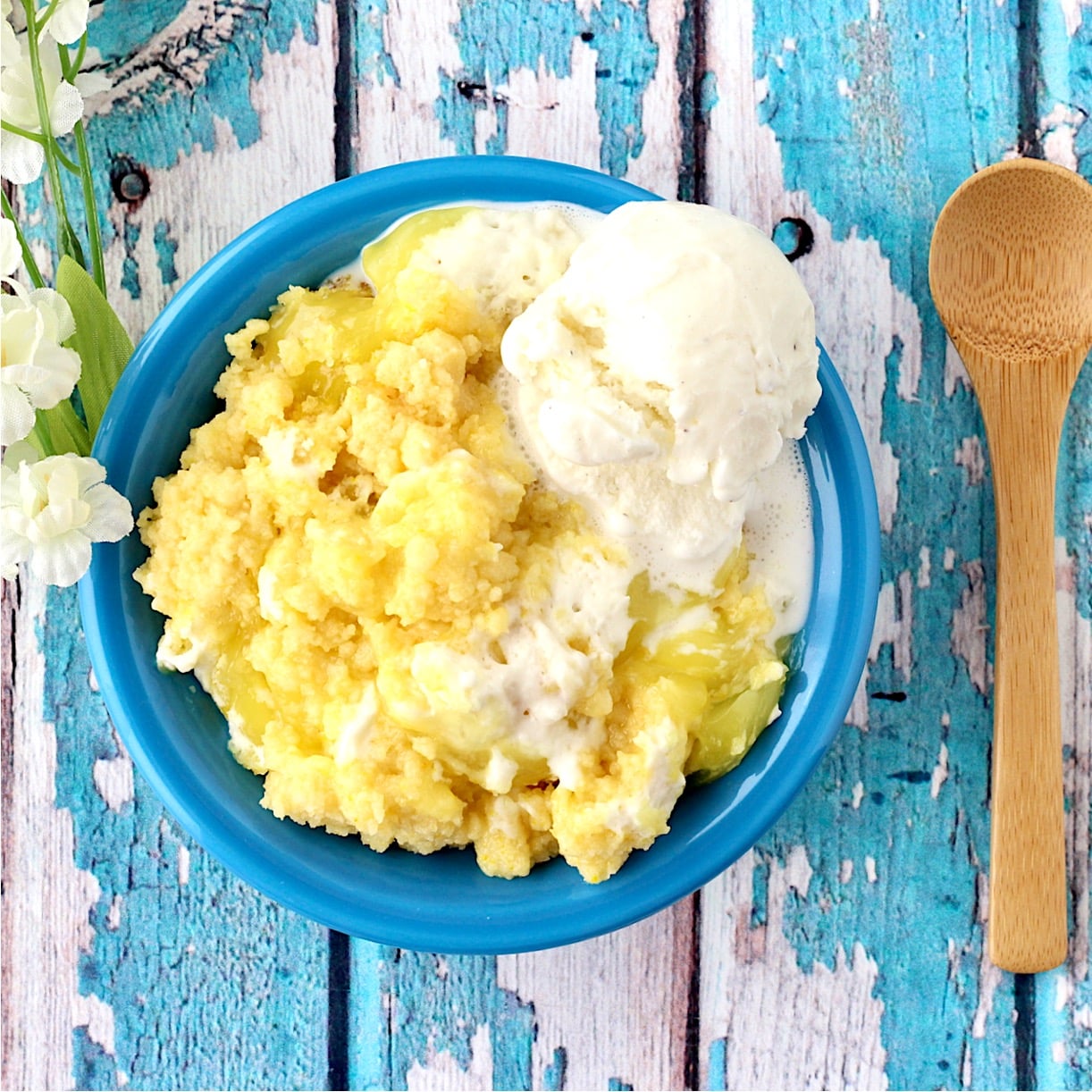 Lemon cream cheese dump cake in bowl with vanilla ice cream and spoon to the side.