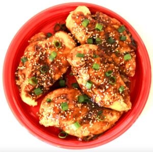Four pieces of Sesame Chicken on plate, garnished with sesame seeds and green onions.
