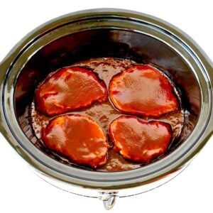 Four pork chops in slow cooker with barbecue sauce.