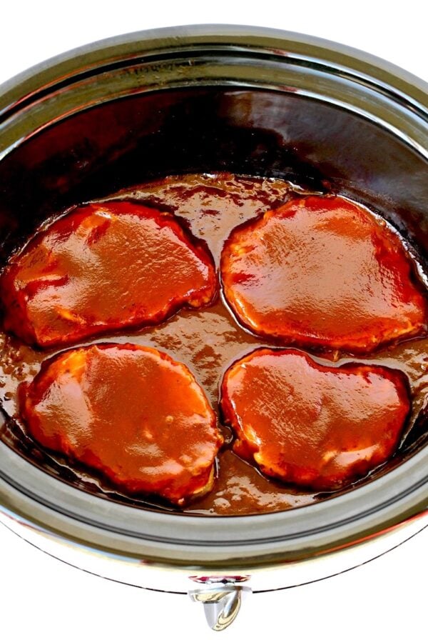 Four pork chops in slow cooker with barbecue sauce.