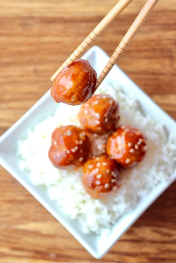 Sweet and Sour meatballs on rice with chopsticks holding one meatball.