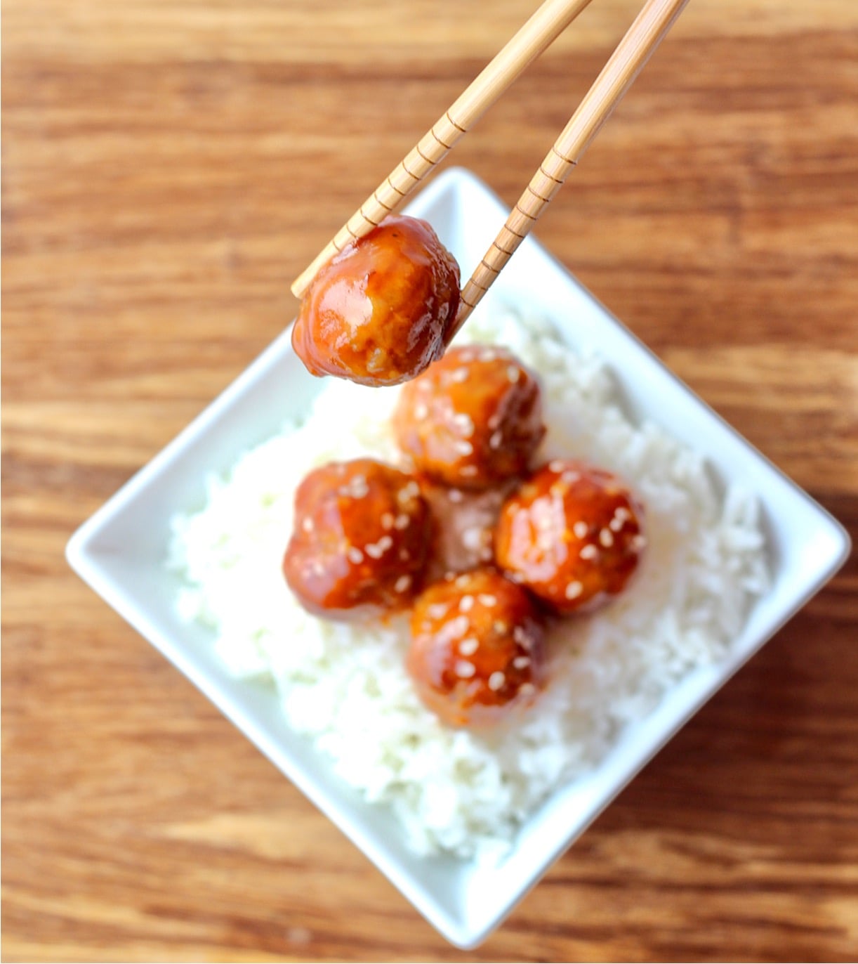 Sweet and Sour meatballs on rice with chopsticks holding one meatball.