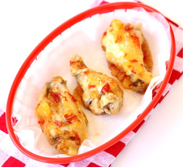 Three chicken wings in basket with Thai sweet chili sauce.