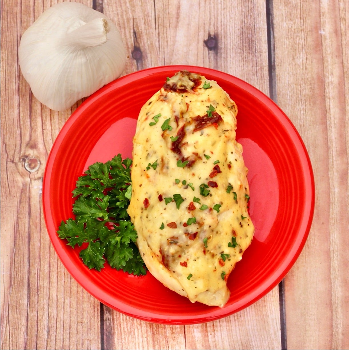 Piece of creamy Tuscan Chicken on plate with garlic and parsley to the side.
