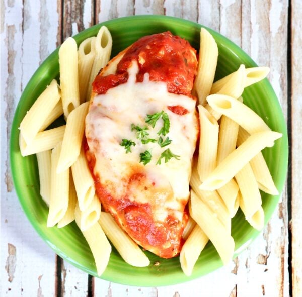 Chicken marinara on plate with mozzarella cheese on top and pasta to the side.