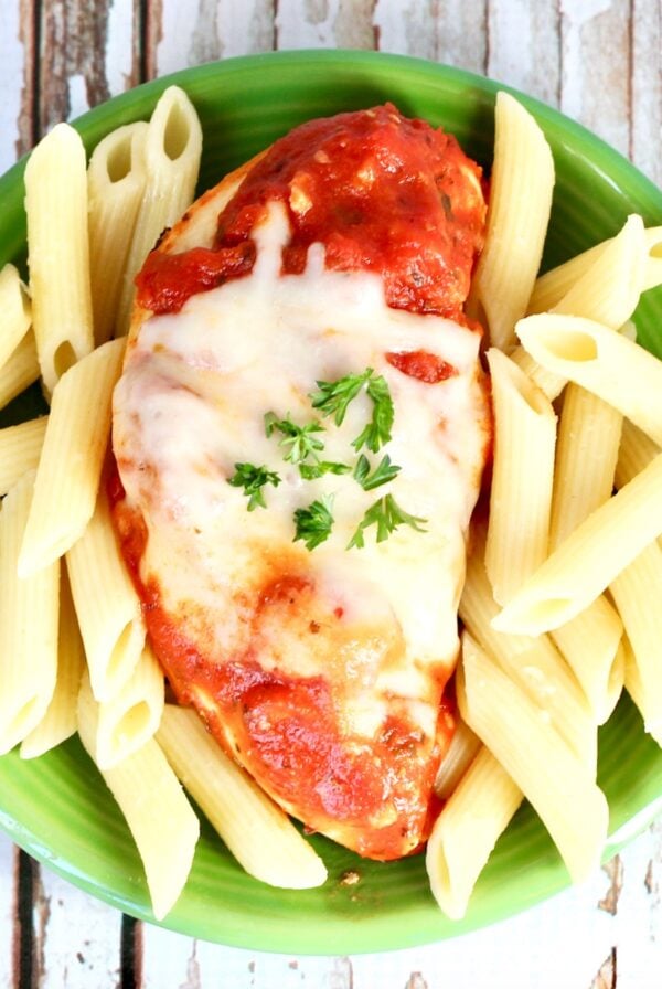 Chicken marinara on plate with mozzarella cheese on top and pasta to the side.