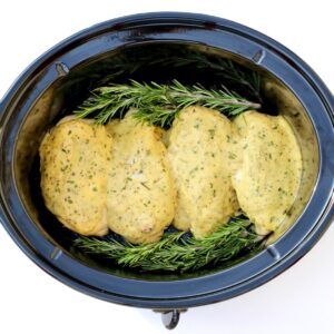 Four pieces of Garlic Herb Chicken in crock pot with rosemary.