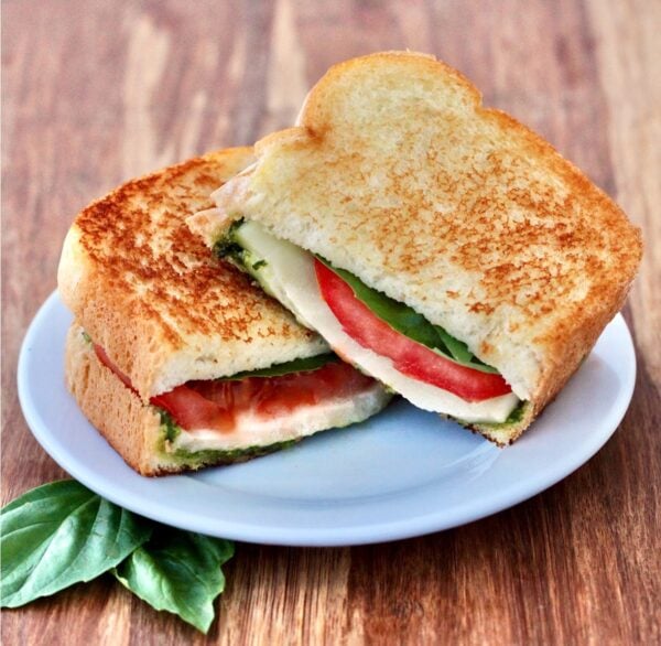 Grilled caprese sandwich cut in half on plate.